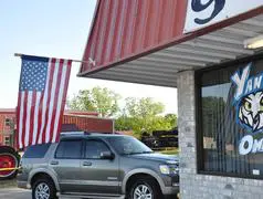 A car parked outside of a store with an american flag hanging from the roof.