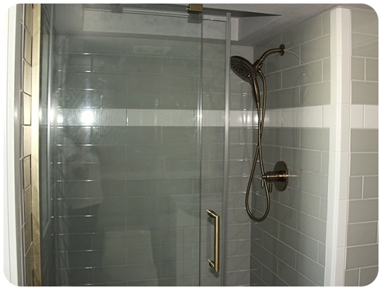 A shower with a glass door and white tile walls.