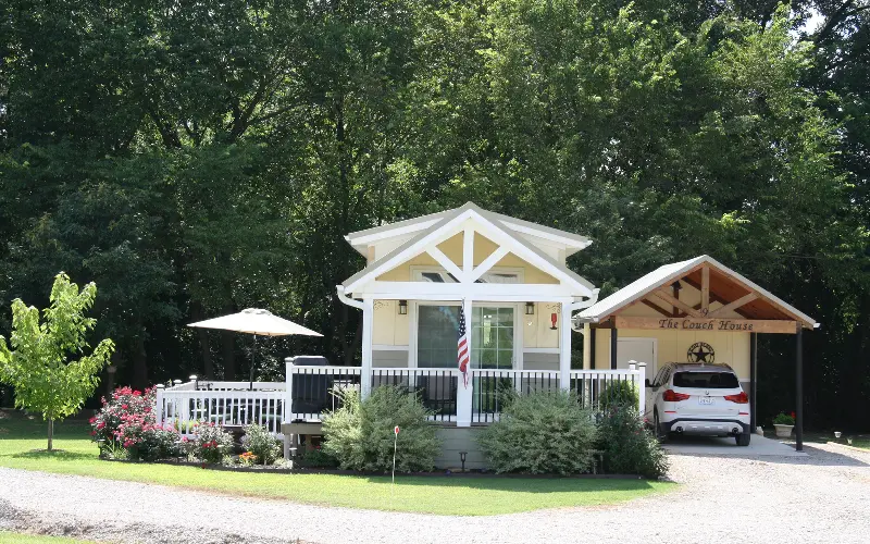 A yellow house with a white porch and a car parked in front of it.