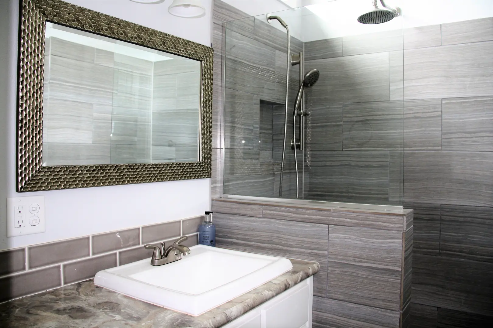 A bathroom with a sink, mirror and shower.