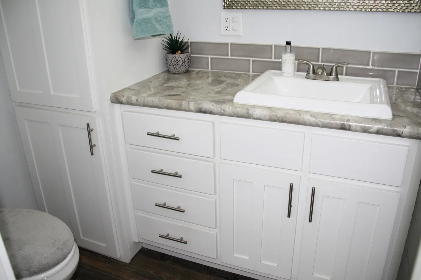 A bathroom with white cabinets and grey counter tops.