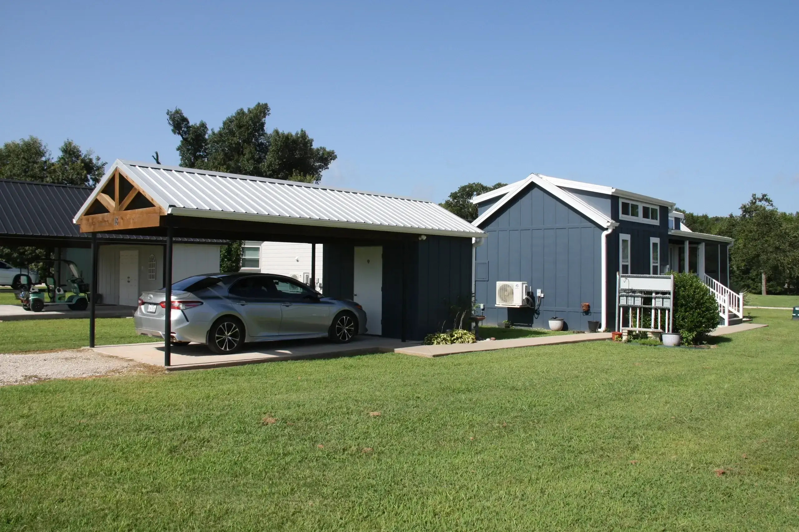 Tiny house with carport on grass lawn.