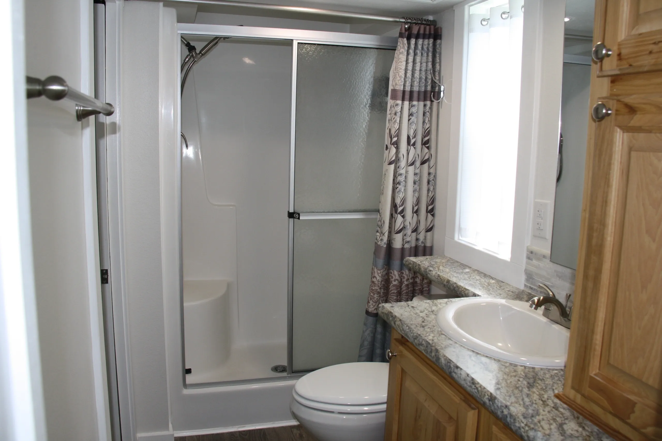 Small bathroom with shower and wooden cabinets.
